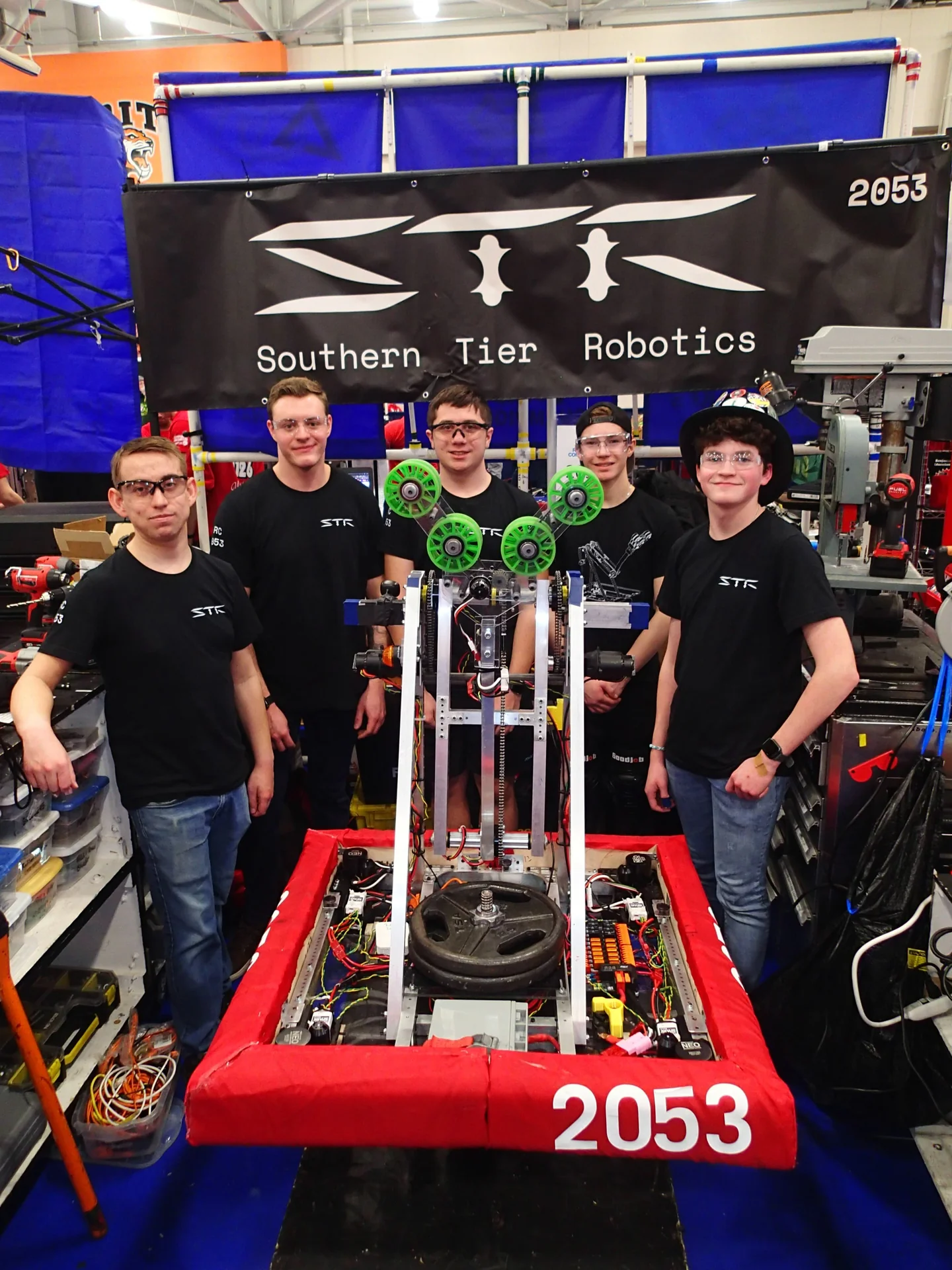 Five students standing behind the robot in the pit at a competition, under the team's banner